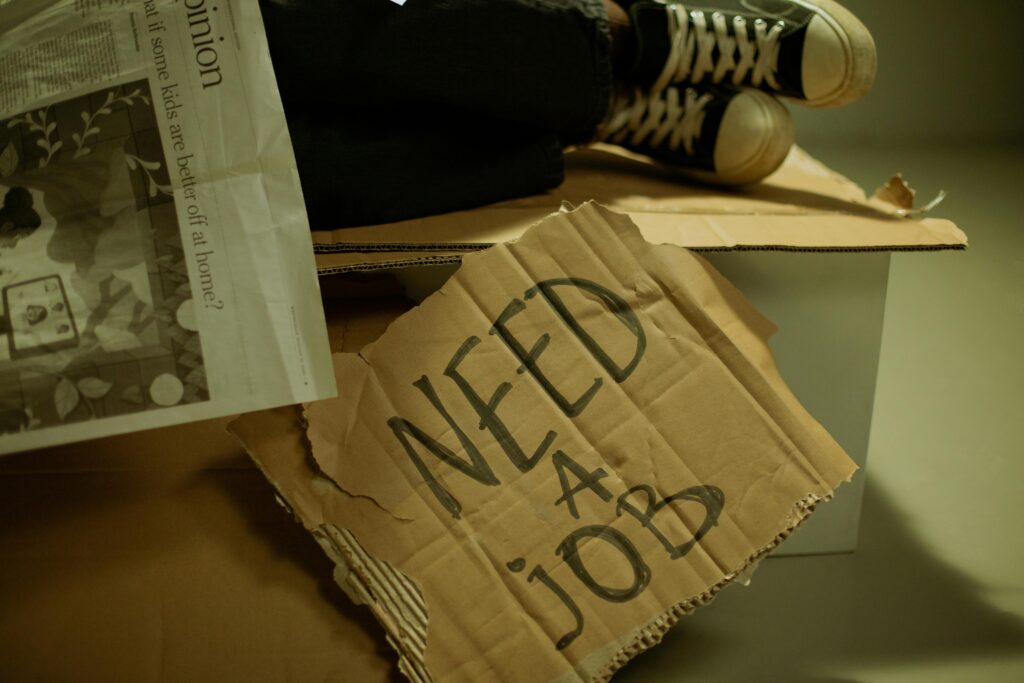 Close-up of a cardboard sign and newspaper depicting joblessness and unemployment.