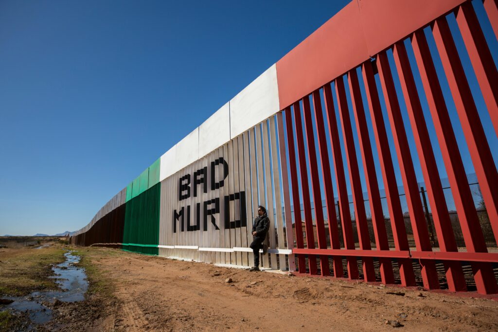 pexels-photo-12330156-12330156 Image of a man standing by the border wall painted with Mexican flag colors in Naco, Sonora, Mexico.