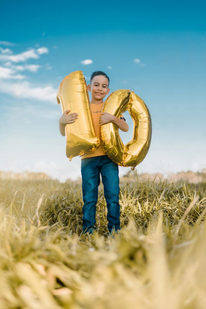 pexels-photo-15306008-15306008 Smiling boy holding gold balloons celebrating 10th birthday in a sunny field in Costa Rica.
