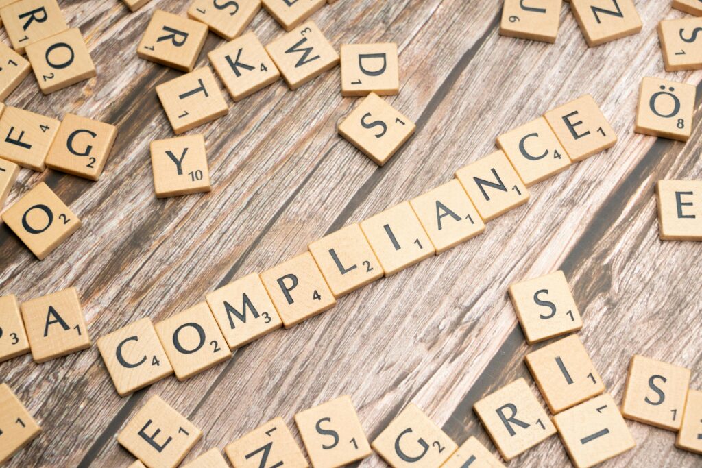 pexels-photo-19825346-19825346 Wooden letter tiles forming the word 'COMPLIANCE' on a rustic wooden background.