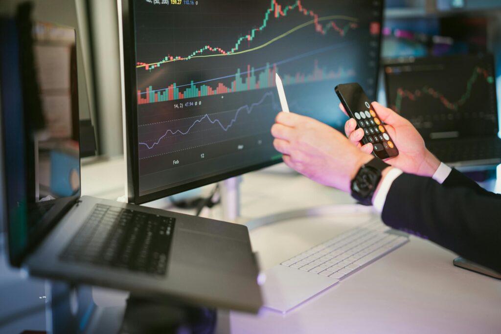 pexels-photo-26745679-26745679 A professional analyzing financial charts on computer monitors and a smartphone, symbolizing digital finance strategies.