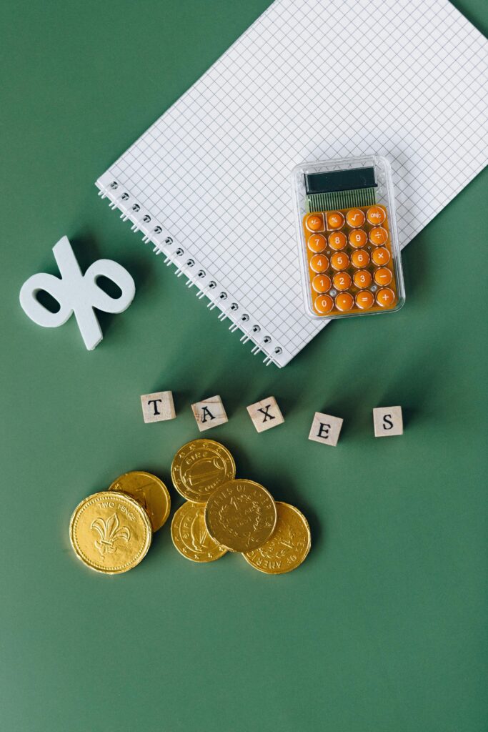 pexels-photo-6863180-6863180 Flat lay of calculator, gold coins, notebook, and tax symbols on a green background.