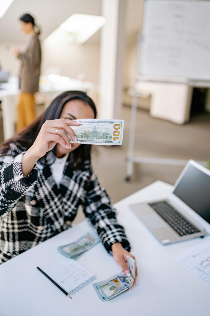 pexels-photo-7691773-7691773 Woman in an office holding a hundred dollar bill, focusing on finances and work environment.