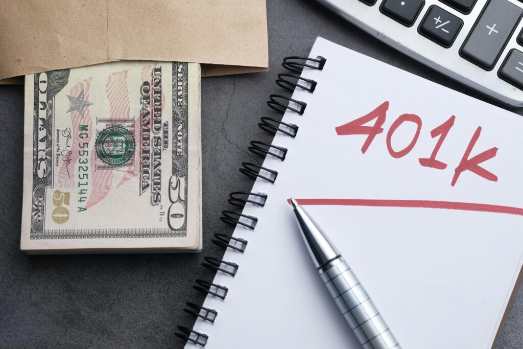 pexels-photo-11350082-11350082 A desk setup with a notebook labeled '401k', a pen, cash, and a calculator representing financial planning.