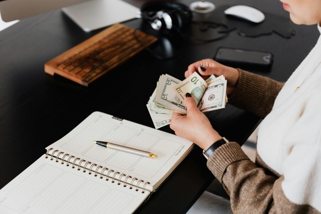 pexels-photo-4475527-4475527 Person counting money at a desk with a planner, showcasing financial management and budgeting in a modern office setting.