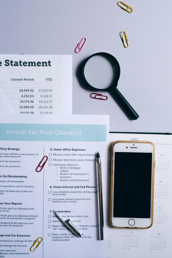 pexels-photo-8962472-8962472 Flat lay of tax documents, magnifying glass, smartphone, and paper clips on a desk.