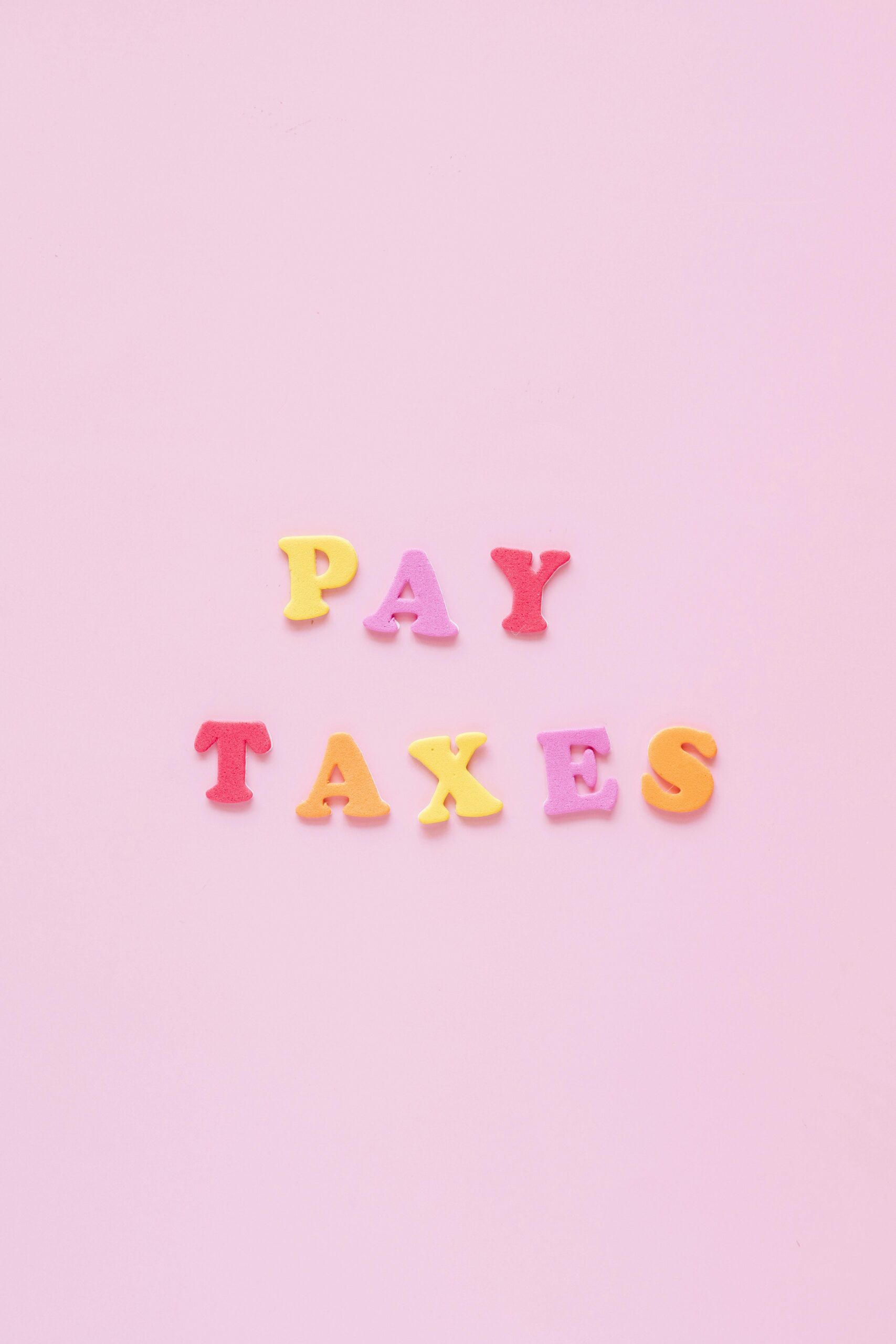 Vibrant letters spelling 'Pay Taxes' on a soft pink backdrop, perfect for financial themes.